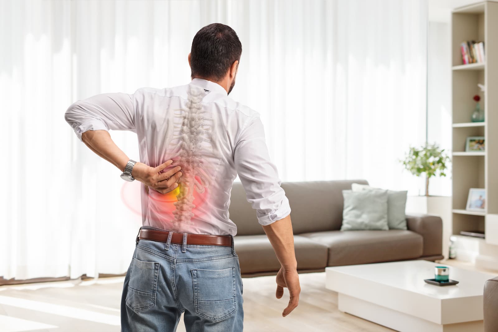 A man viewed from behind clutching his lower back, featuring a transparent overlay of a human spine with a glowing red and yellow area indicating lumbar pain.